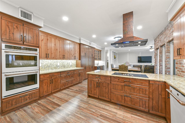 kitchen with island exhaust hood, black electric stovetop, double wall oven, stainless steel dishwasher, and light hardwood / wood-style flooring