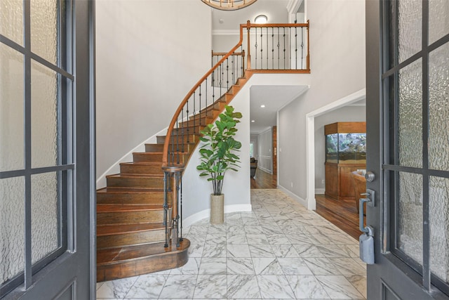 entryway with wood-type flooring, crown molding, and a high ceiling