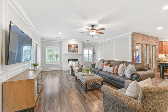 living room with dark hardwood / wood-style floors, ceiling fan, ornamental molding, a textured ceiling, and a fireplace