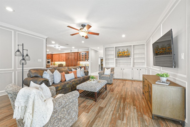 living room featuring built in shelves, light hardwood / wood-style floors, ceiling fan, and ornamental molding