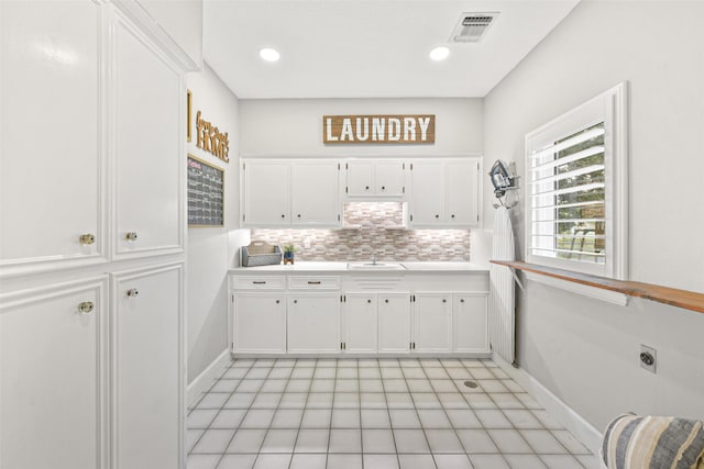 kitchen featuring tasteful backsplash, white cabinetry, sink, and light tile patterned floors