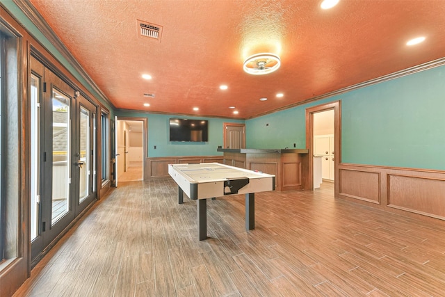 game room with hardwood / wood-style floors, ornamental molding, a textured ceiling, and french doors