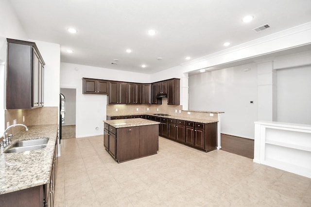 kitchen featuring dark brown cabinetry, light stone counters, sink, and a kitchen island