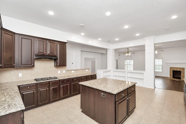 kitchen with dark brown cabinets, a center island, ornamental molding, and a tiled fireplace