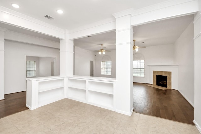 unfurnished living room with ceiling fan, decorative columns, crown molding, light hardwood / wood-style floors, and a tiled fireplace