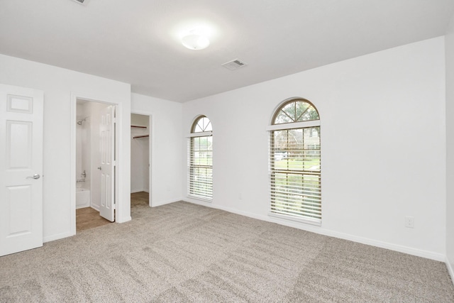 unfurnished bedroom featuring a walk in closet, a closet, ensuite bath, and light colored carpet