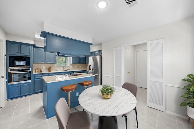 kitchen with tasteful backsplash, stainless steel appliances, sink, blue cabinetry, and light tile patterned floors