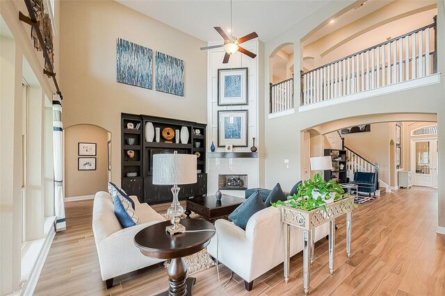 living room with a high ceiling, a large fireplace, ceiling fan, and hardwood / wood-style floors