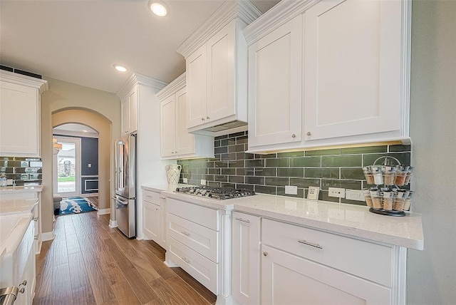 kitchen with light stone countertops, tasteful backsplash, light wood-type flooring, white cabinets, and appliances with stainless steel finishes