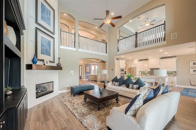 living room with a high ceiling, light wood-type flooring, a large fireplace, and ceiling fan