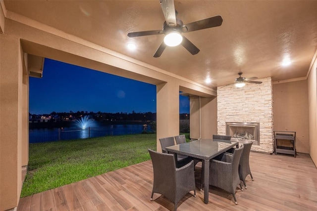 deck at twilight with a lawn, an outdoor stone fireplace, and a water view