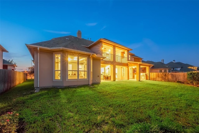 back house at dusk with a lawn and a balcony