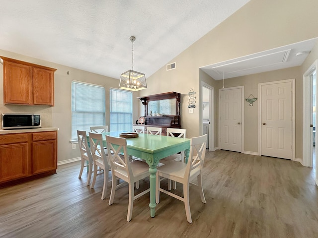 dining room featuring a textured ceiling, light wood-type flooring, high vaulted ceiling, and a notable chandelier