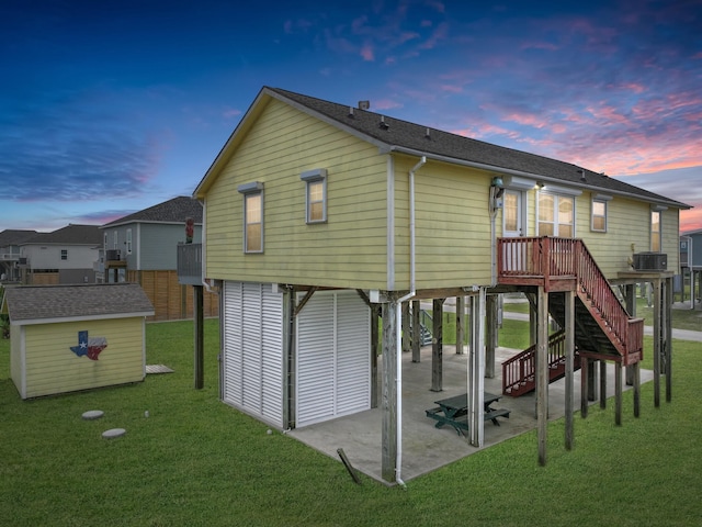 back house at dusk featuring a yard, central AC, a storage unit, and a patio area