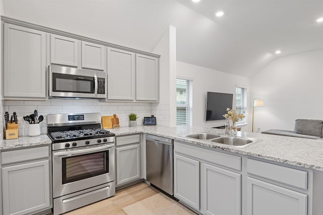 kitchen with decorative backsplash, stainless steel appliances, vaulted ceiling, sink, and light hardwood / wood-style floors