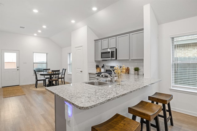 kitchen with stainless steel appliances, tasteful backsplash, light hardwood / wood-style flooring, kitchen peninsula, and lofted ceiling