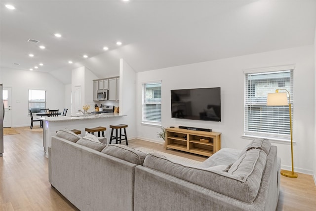 living room with plenty of natural light, lofted ceiling, and light hardwood / wood-style flooring