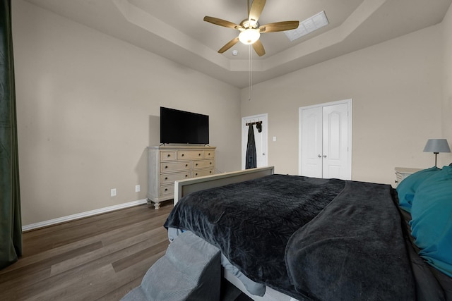 bedroom with ceiling fan, dark hardwood / wood-style floors, a closet, and a tray ceiling