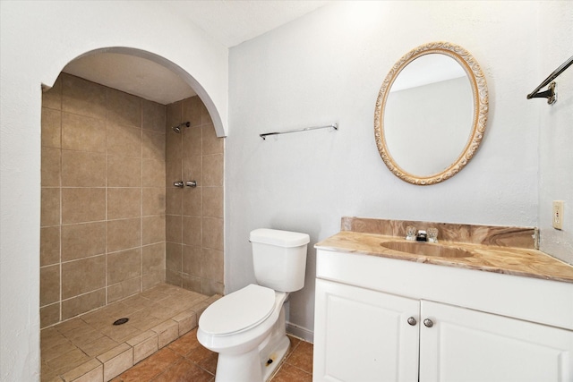 bathroom with a tile shower, tile patterned flooring, vanity, and toilet