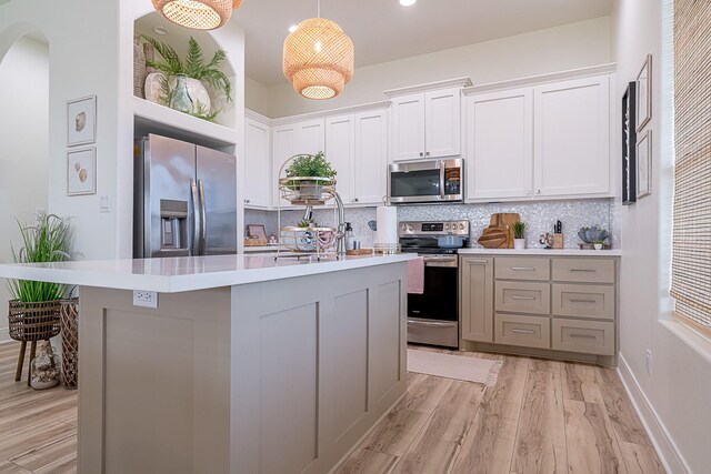 kitchen featuring white cabinetry, stainless steel appliances, light hardwood / wood-style floors, decorative light fixtures, and decorative backsplash