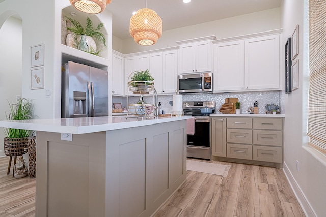 kitchen with backsplash, appliances with stainless steel finishes, white cabinets, a kitchen island with sink, and decorative light fixtures