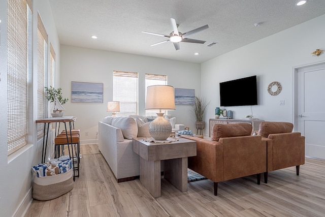 living room featuring ceiling fan, a textured ceiling, and light wood-type flooring