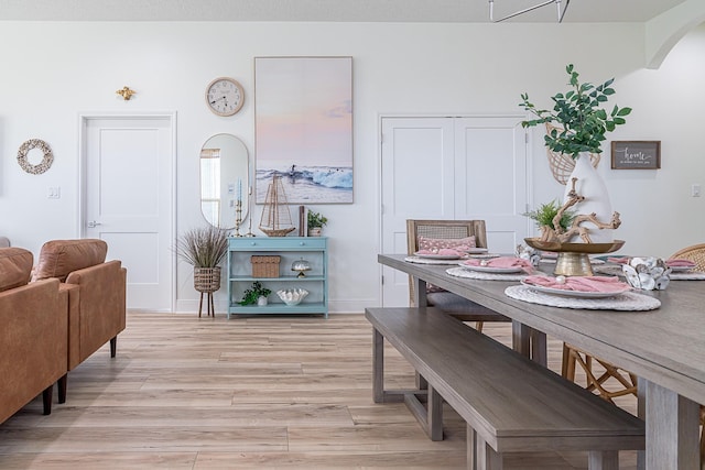 dining space featuring arched walkways, baseboards, and light wood-style floors
