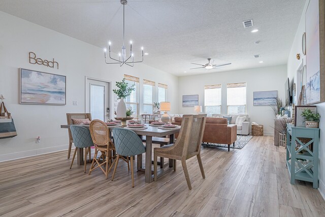 dining area with ceiling fan with notable chandelier, light wood-type flooring, and a textured ceiling