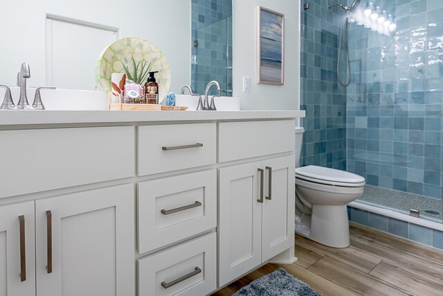 bathroom featuring toilet, vanity, wood-type flooring, and tiled shower