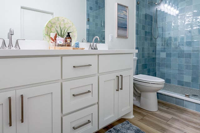 bathroom with toilet, hardwood / wood-style floors, vanity, and tiled shower