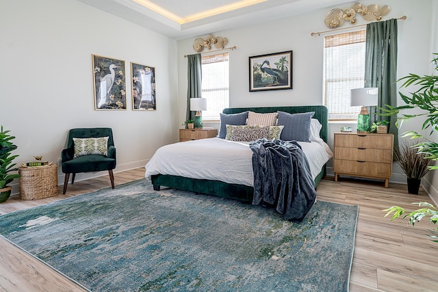 bedroom featuring a tray ceiling, light hardwood / wood-style flooring, and multiple windows