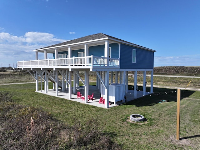 rear view of property featuring a patio area, a fire pit, a deck, a yard, and roof with shingles