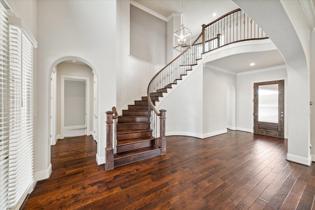 entrance foyer with dark wood-type flooring, a chandelier, ornamental molding, and a wealth of natural light