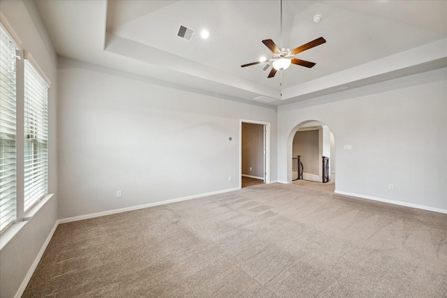 empty room featuring ceiling fan, a tray ceiling, and plenty of natural light