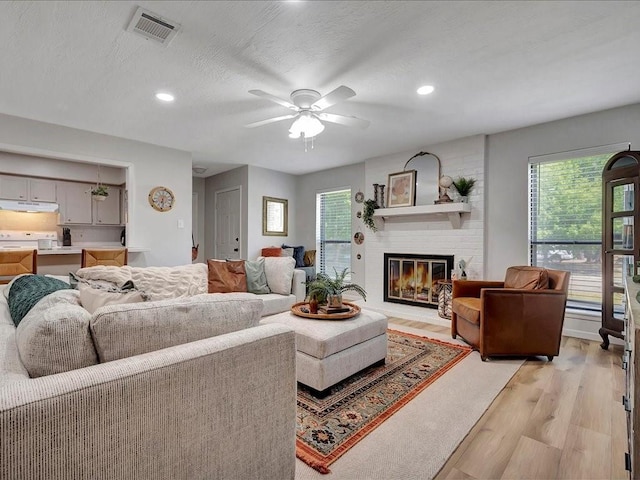 living room with a textured ceiling, ceiling fan, light wood-type flooring, and a fireplace