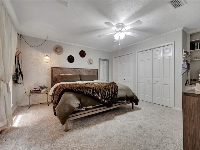 carpeted bedroom with a textured ceiling, ceiling fan, crown molding, and two closets