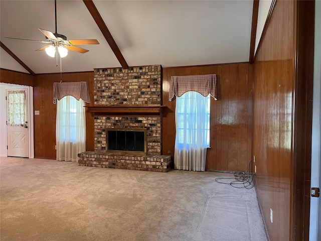 unfurnished living room with a wealth of natural light, carpet floors, lofted ceiling with beams, and wood walls