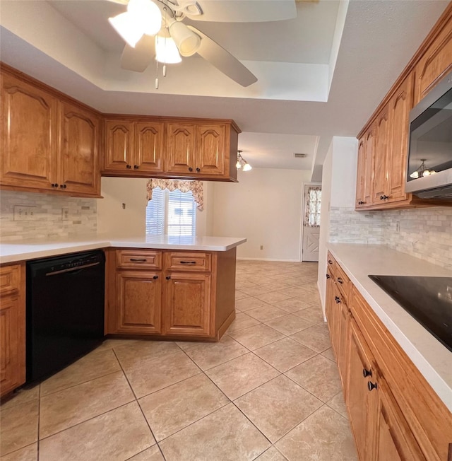 kitchen with kitchen peninsula, tasteful backsplash, a tray ceiling, and black appliances