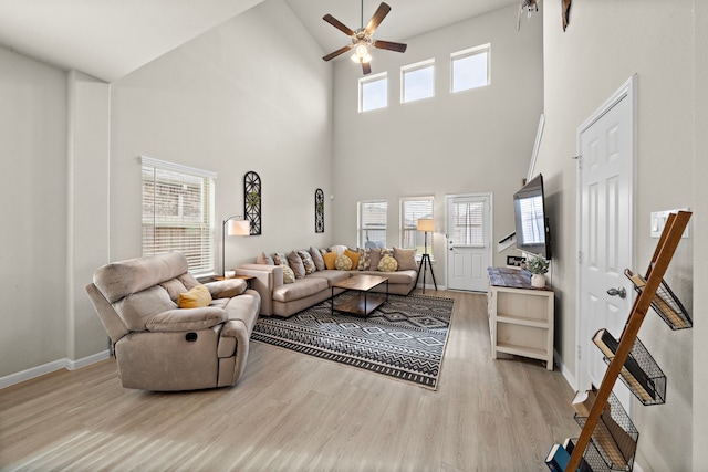 living room with a towering ceiling, light hardwood / wood-style floors, and ceiling fan