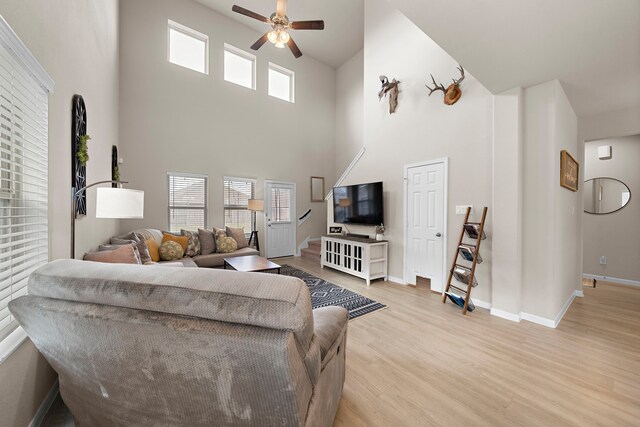 living room featuring ceiling fan, light hardwood / wood-style floors, and a high ceiling