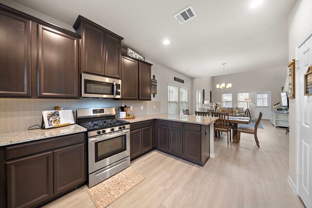 kitchen with kitchen peninsula, stainless steel appliances, a chandelier, and light hardwood / wood-style floors