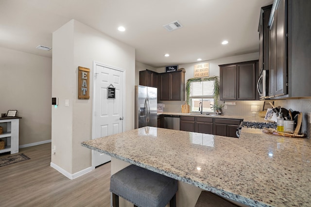 kitchen featuring kitchen peninsula, stainless steel appliances, light stone counters, and light hardwood / wood-style floors