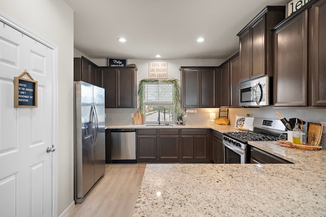 kitchen with sink, appliances with stainless steel finishes, dark brown cabinets, light hardwood / wood-style floors, and light stone counters