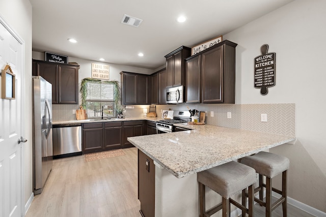 kitchen with a kitchen breakfast bar, light hardwood / wood-style flooring, appliances with stainless steel finishes, light stone counters, and kitchen peninsula