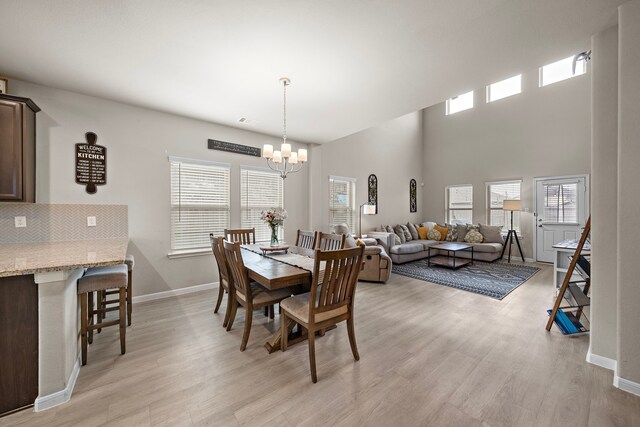 dining room featuring a towering ceiling, light wood-type flooring, and an inviting chandelier