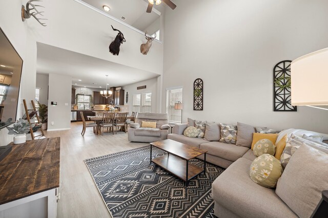 living room with hardwood / wood-style floors, ceiling fan with notable chandelier, and a high ceiling