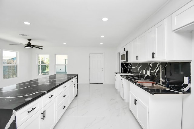 kitchen featuring white cabinets, decorative backsplash, ceiling fan, and dark stone counters