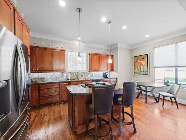 kitchen with stainless steel fridge, hardwood / wood-style flooring, a kitchen island, hanging light fixtures, and a breakfast bar area