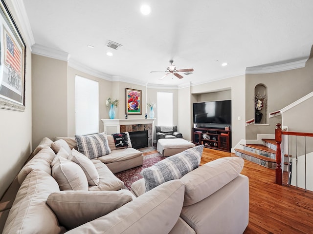 living room with a tiled fireplace, crown molding, ceiling fan, and hardwood / wood-style flooring