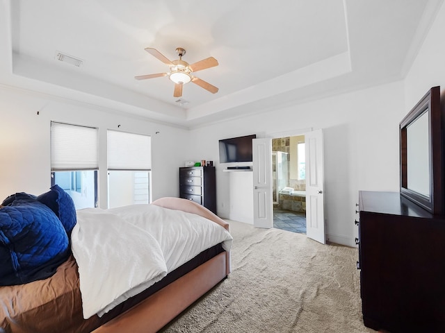 bedroom featuring a tray ceiling, ceiling fan, light colored carpet, and ensuite bathroom